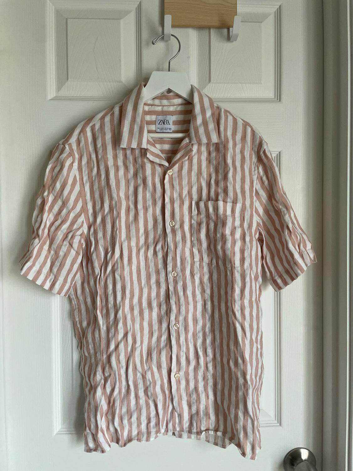 White and pink striped shirt hanging on a white hanger over a white door. Label visible: Zara.