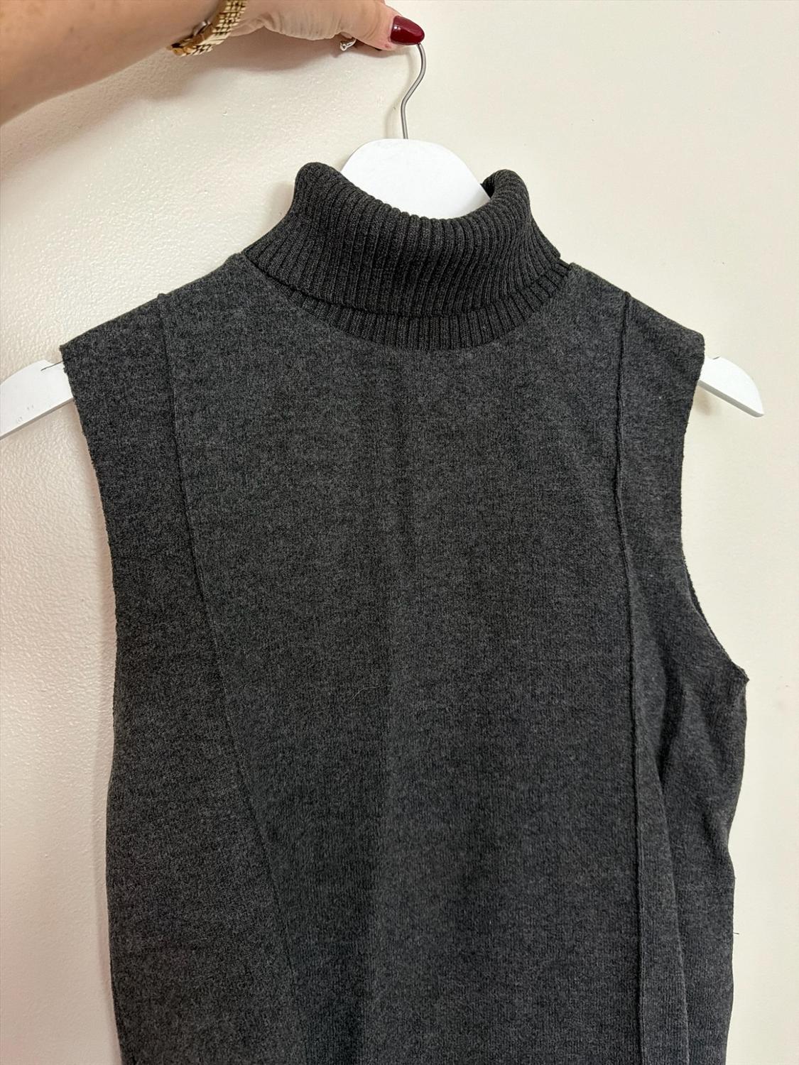 Here’s the rephrased sentence: A gray knit garment, sleeveless and with a high collar, hanging from a white hook held by a hand.