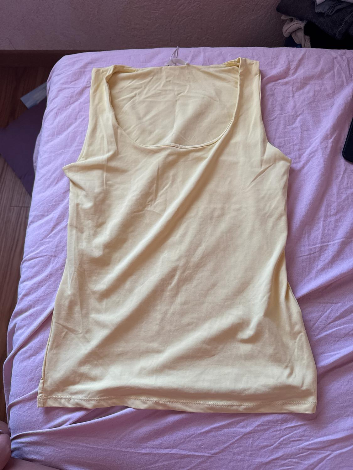 Light yellow basic vest top, laid out on a bed with pink sheets in a casual setting.