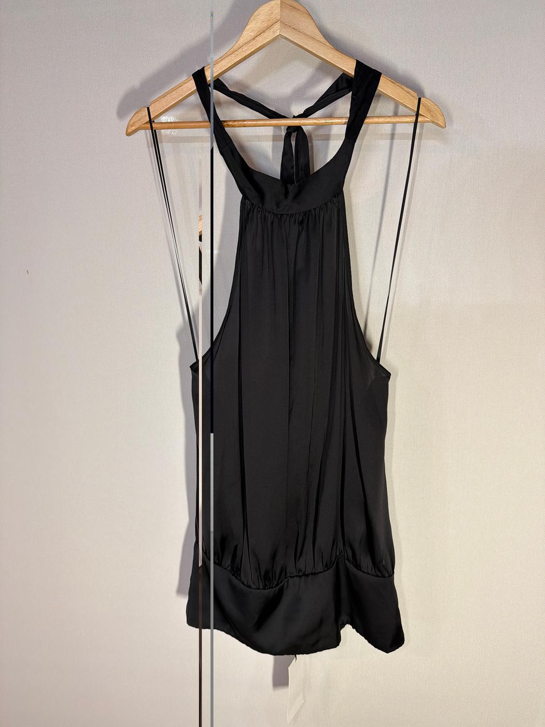 Black sleeveless blouse hanging on a wooden hanger, with a halter neck and bow detail on the back, against a light background.