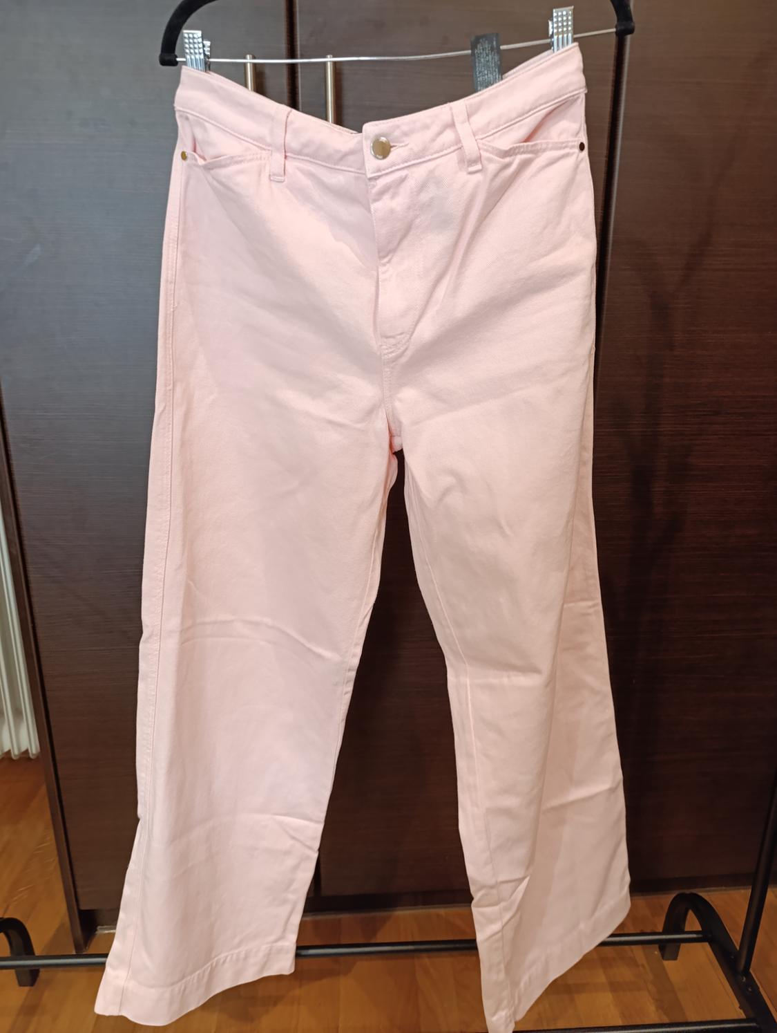 Light pink trousers hanging on a metal clothes rack, dark wood background.