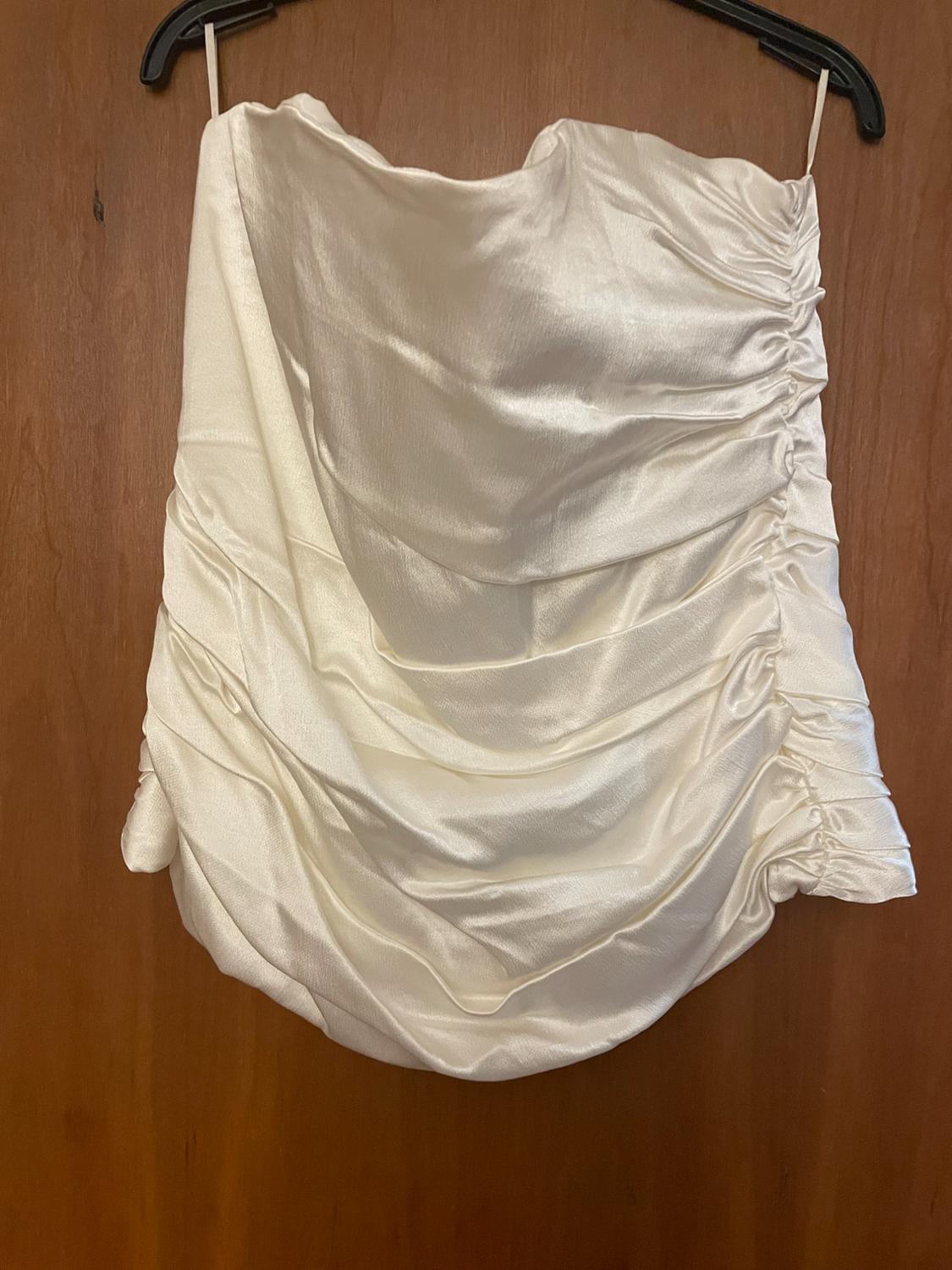 White satin draped top hanging on a black hanger over a wooden door.