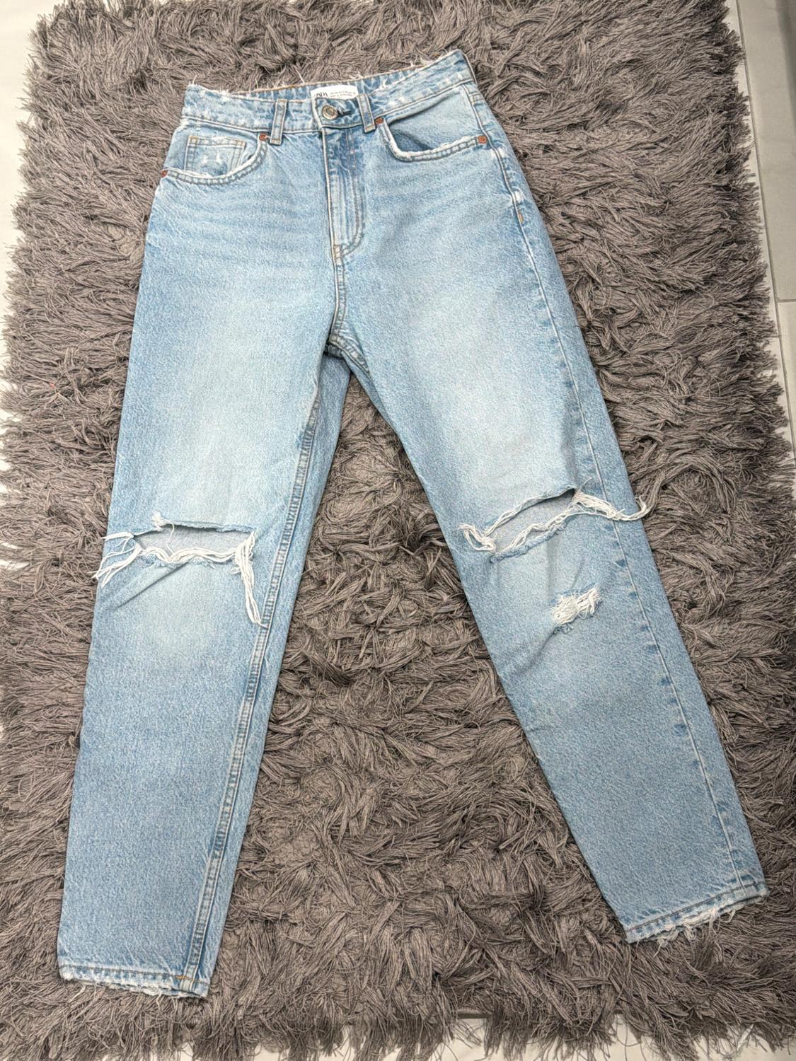 Distressed blue jeans with knee rips, placed on a fuzzy gray textured rug.