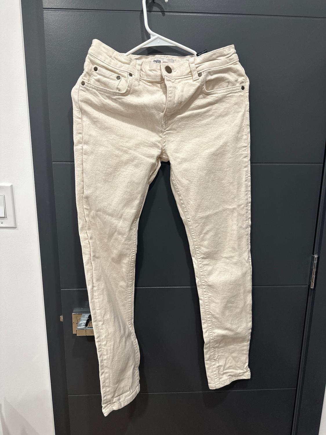 Beige pants hanging on a white hanger over a dark door. Classic design with front and back pockets.