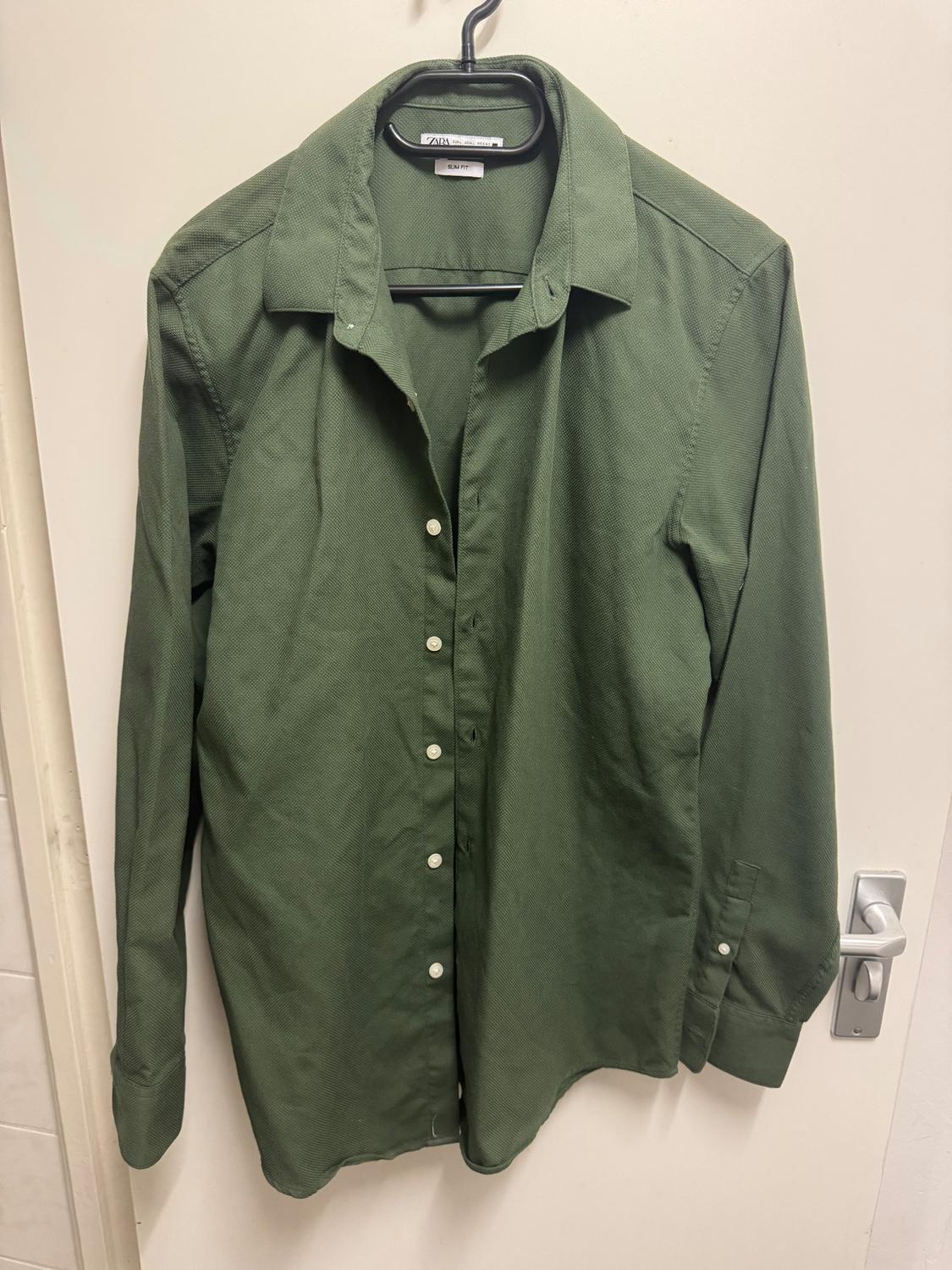 Long-sleeved green shirt hanging on a black hanger over a white door. White buttons visible on the front.