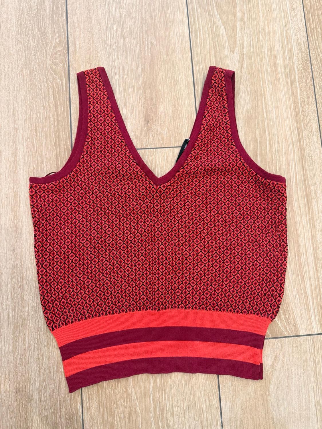 Sleeveless knitted V-neck top, red and black geometric print, and striped hem, set against a light wood background.