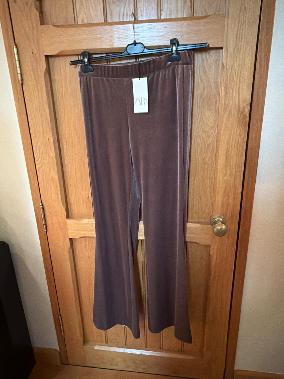 Brown velvet trousers hanging on a wooden door with a label that says "ZARA".