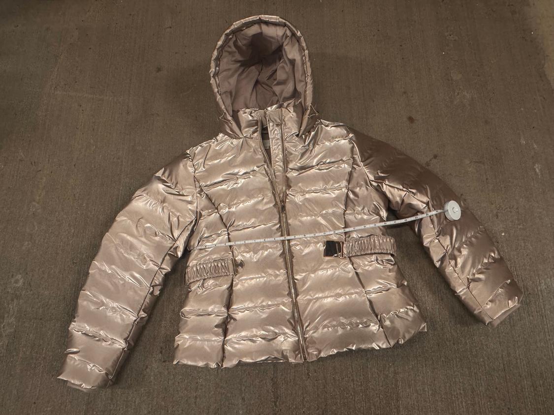 Metallic puffer jacket with a hood on a brown floor. White measuring tape measures the width of the jacket.