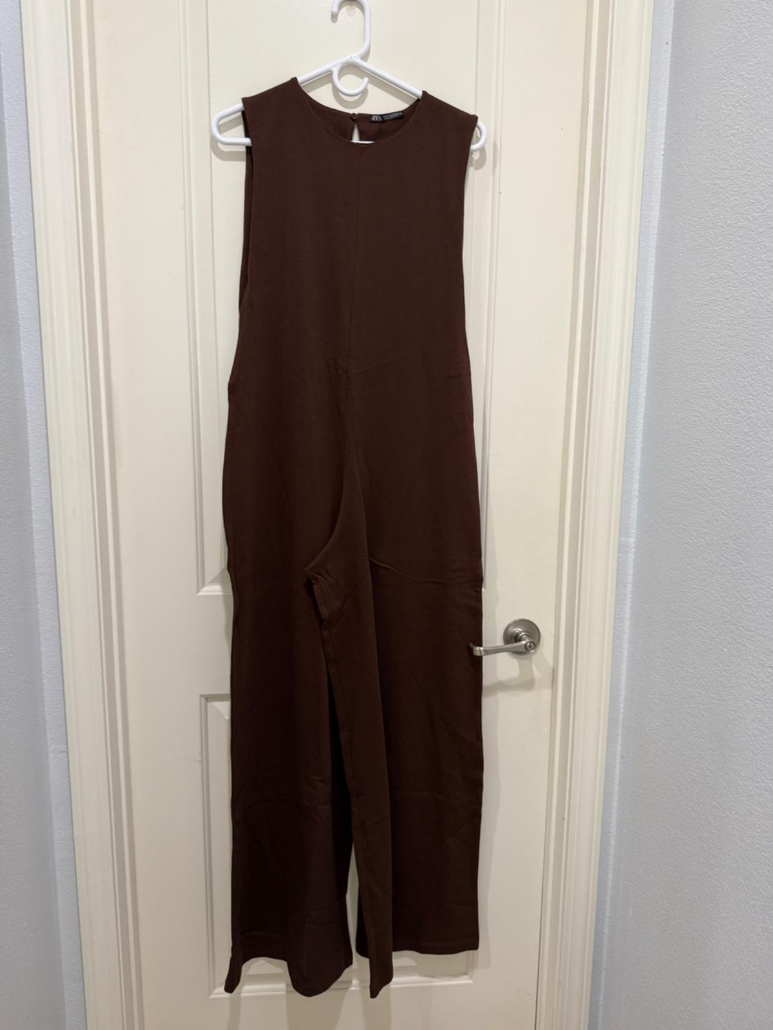 Sleeveless brown jumpsuit hanging on a white hanger over a white door.
