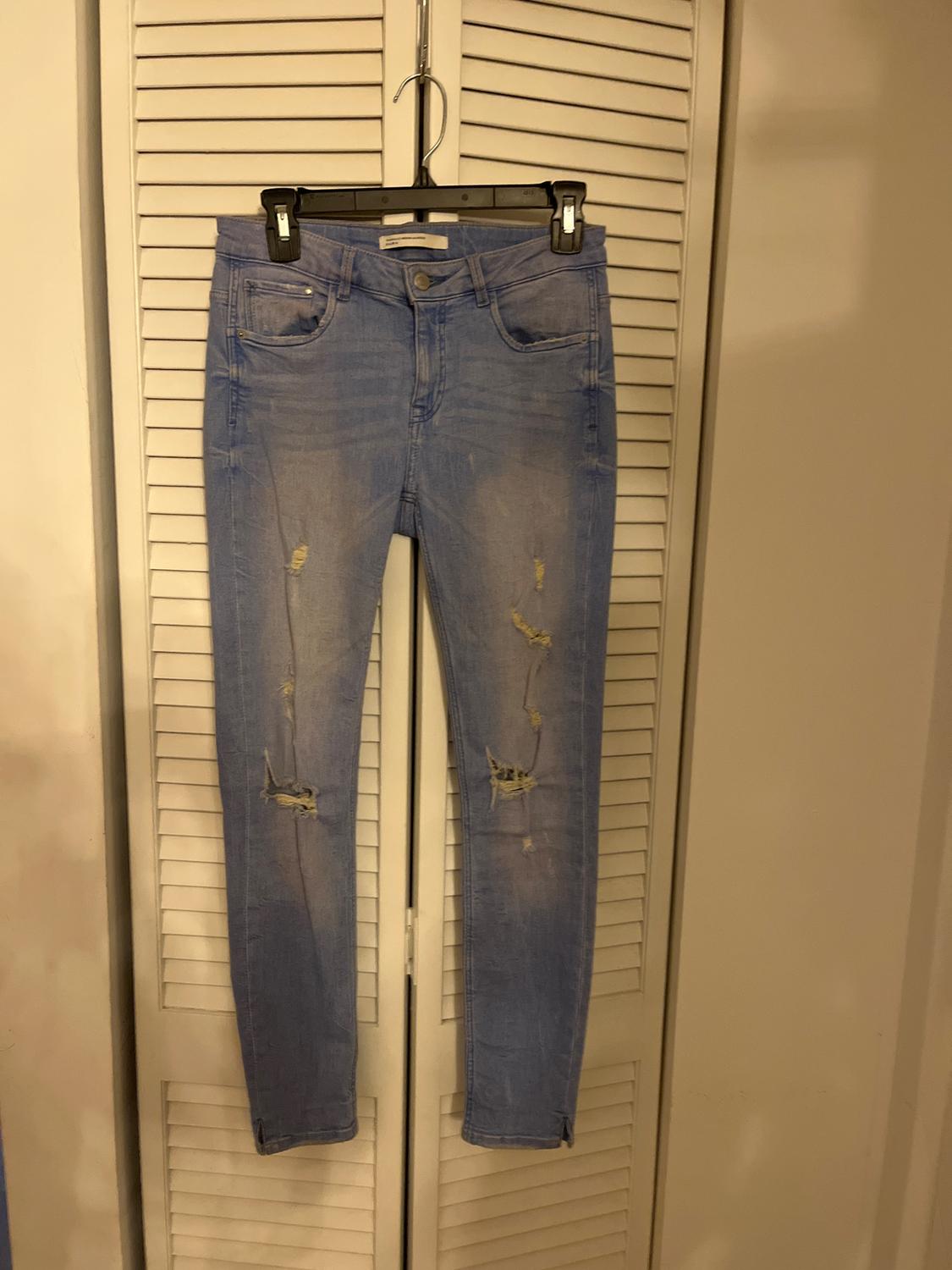 Distressed blue jeans hanging on a black hanger in front of a white slatted door.