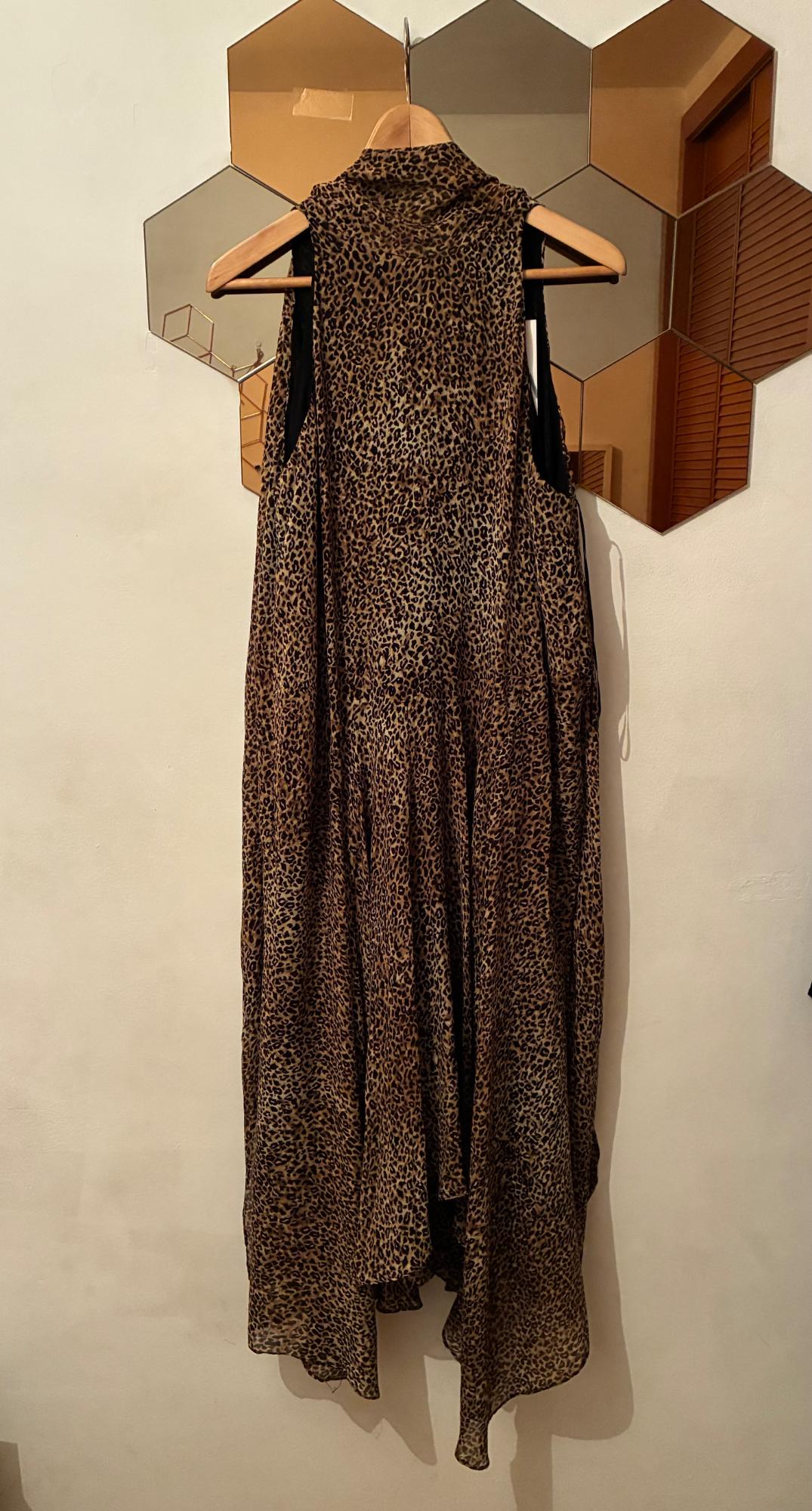 Sleeveless animal print maxi dress hanging on a wooden hanger against a white wall with a hexagonal mirror.