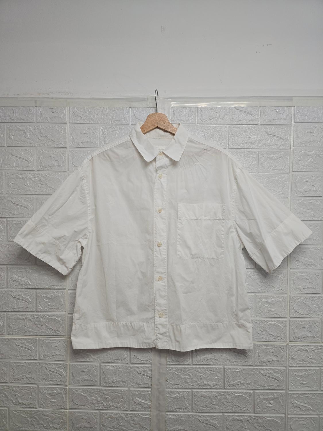Short-sleeved white shirt hanging on a wooden hanger over a textured grey tiled wall.