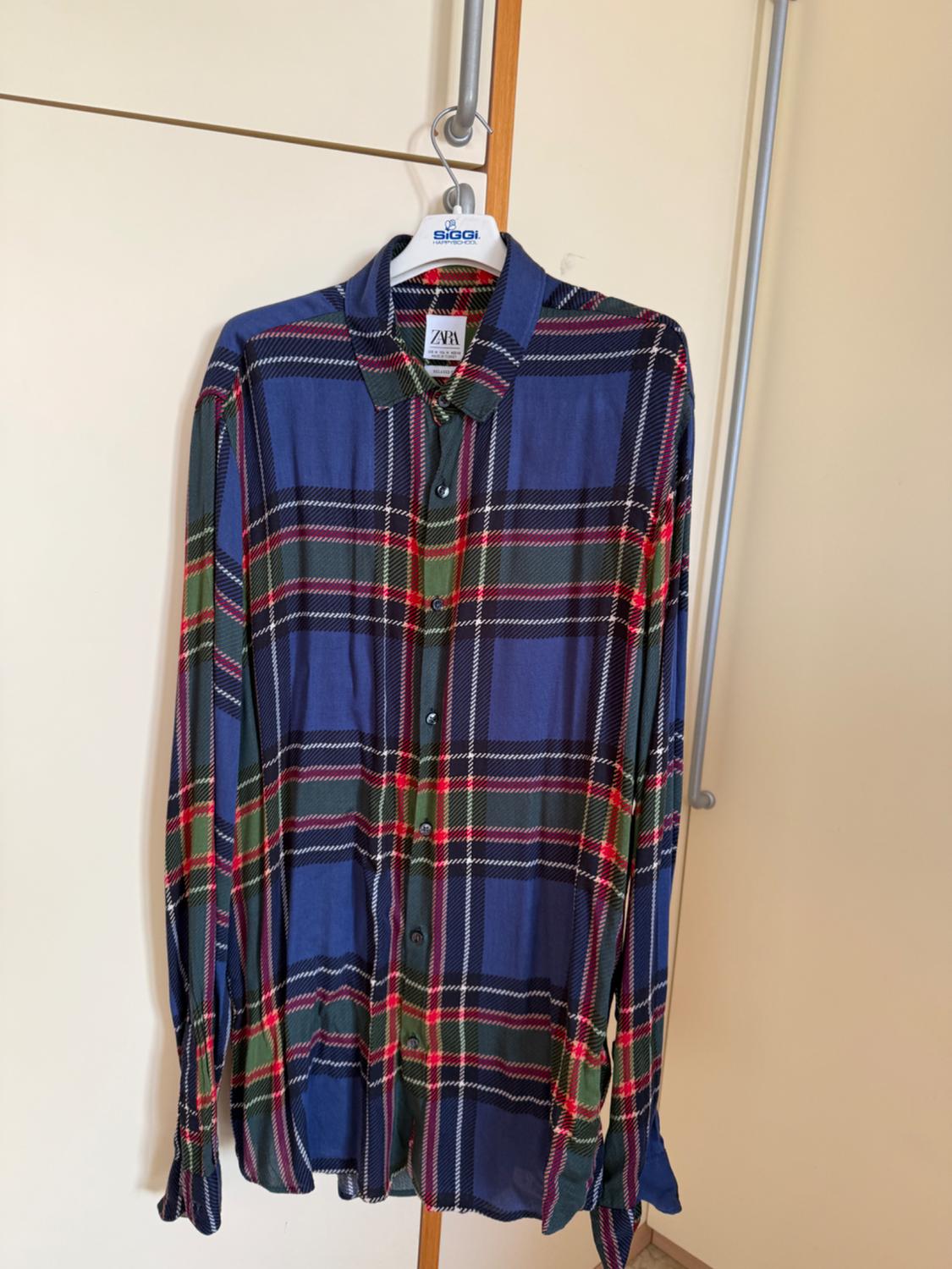 Blue, green, and red checked shirt hanging on a white hanger with the "SIGGI" brand visible in a light-coloured wardrobe.