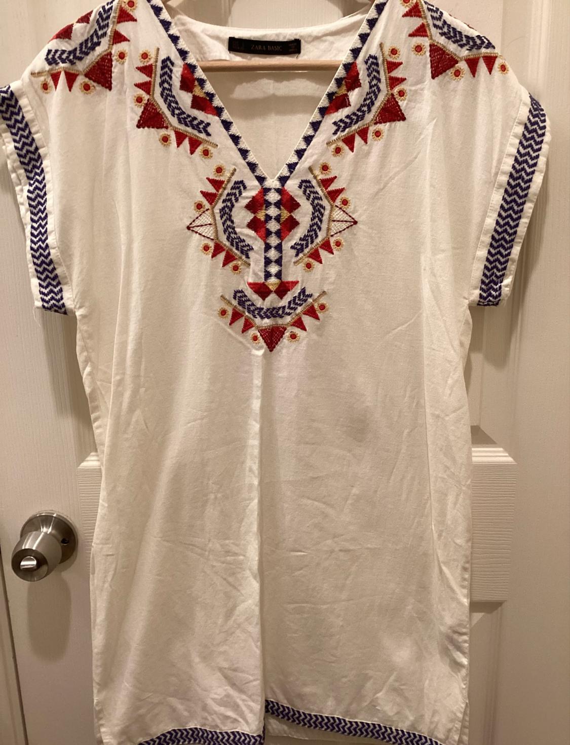 Front view of a white dress with red and blue geometric embroidery on the chest and sleeves.