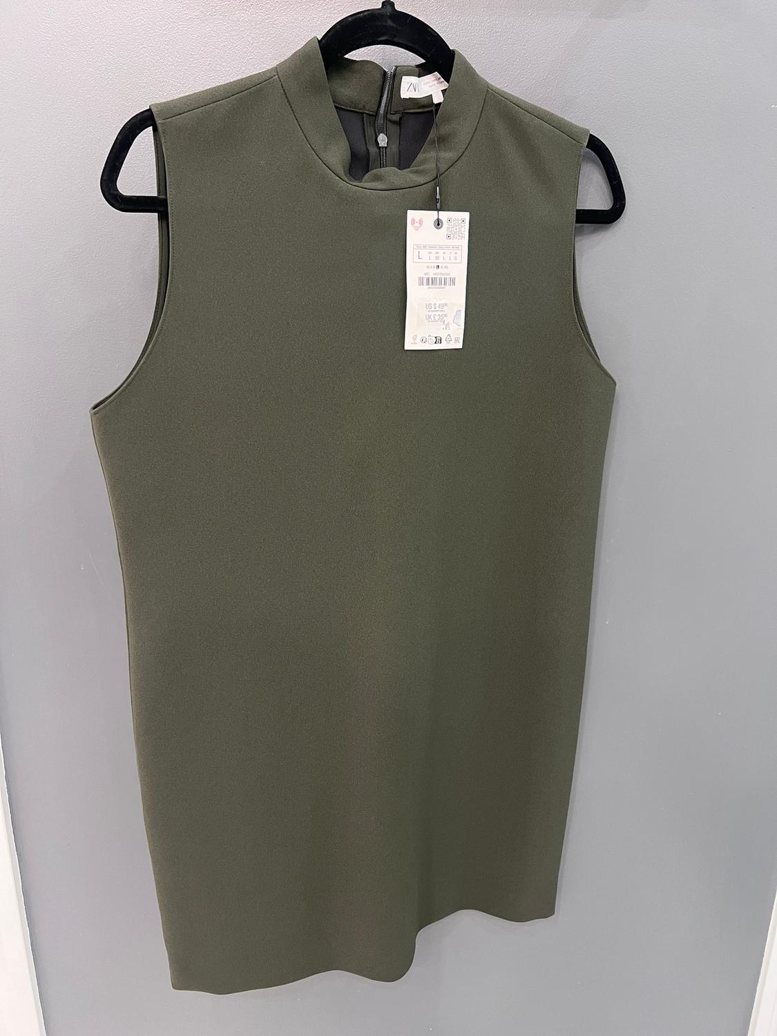 Olive green sleeveless dress on a black hanger, with a visible price tag. Light gray background.