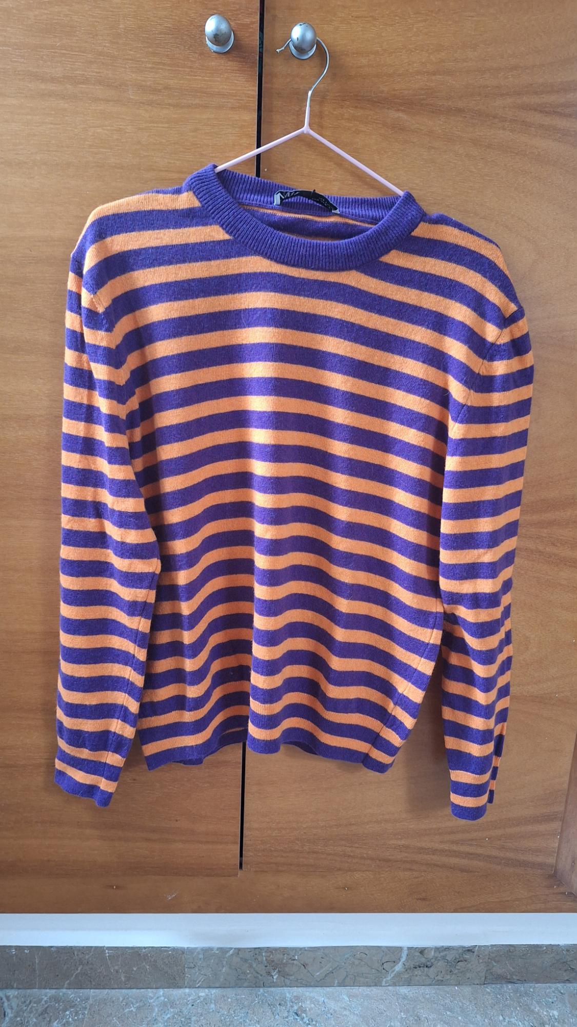 Purple and orange striped jumper hanging on a hanger in front of a wooden wardrobe.