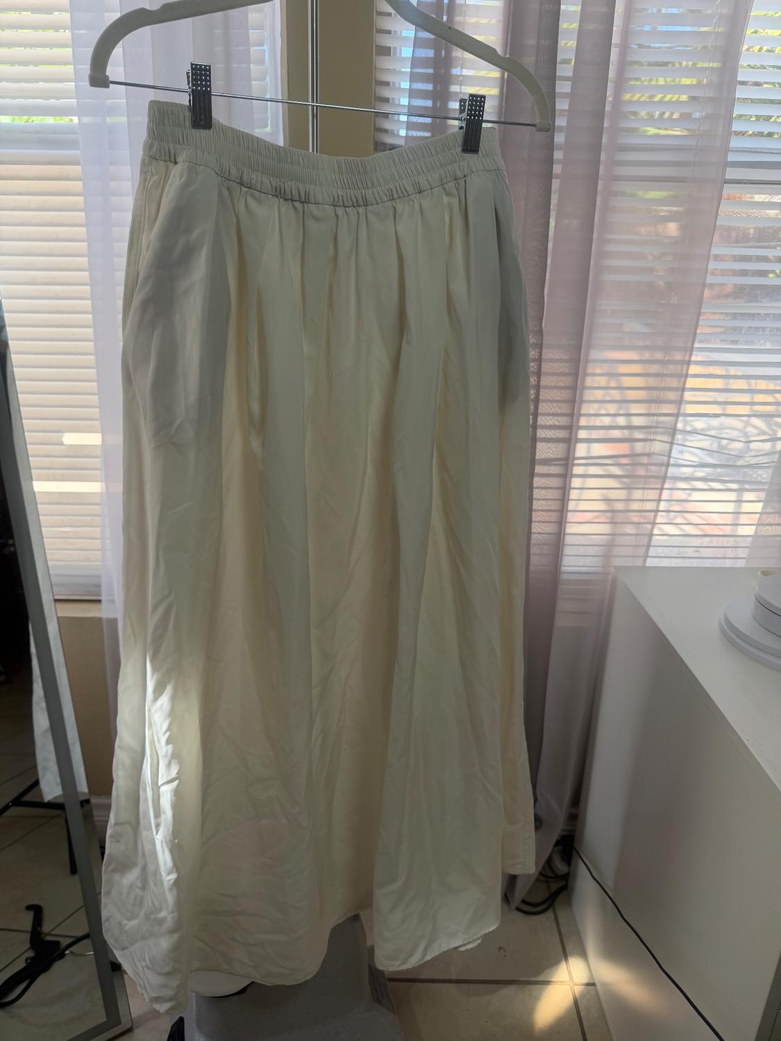 Long white skirt hanging on a hanger in front of a window with translucent curtains. Natural light illuminates the scene.