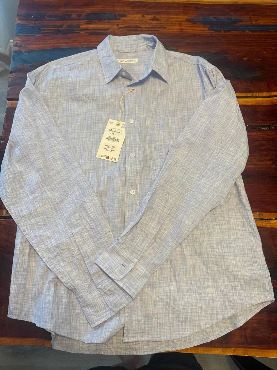Light blue textured long-sleeve button-down shirt with a label, on a wooden table.