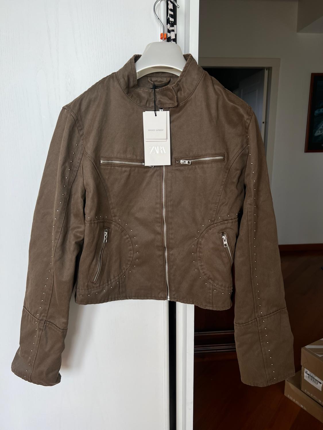 Brown jacket with zips and studs hanging on a door. Label with the text WASHED GARMENT ZARA.