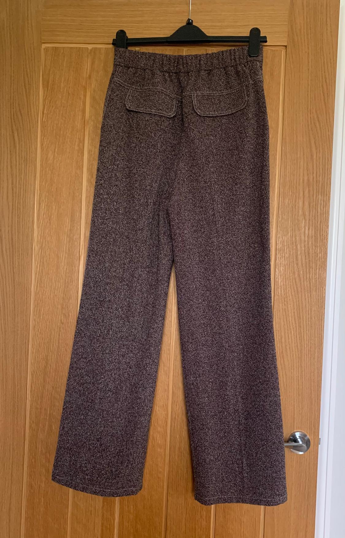 Brown wool trousers hanging on a wooden door, with back pockets and an elasticated waist.