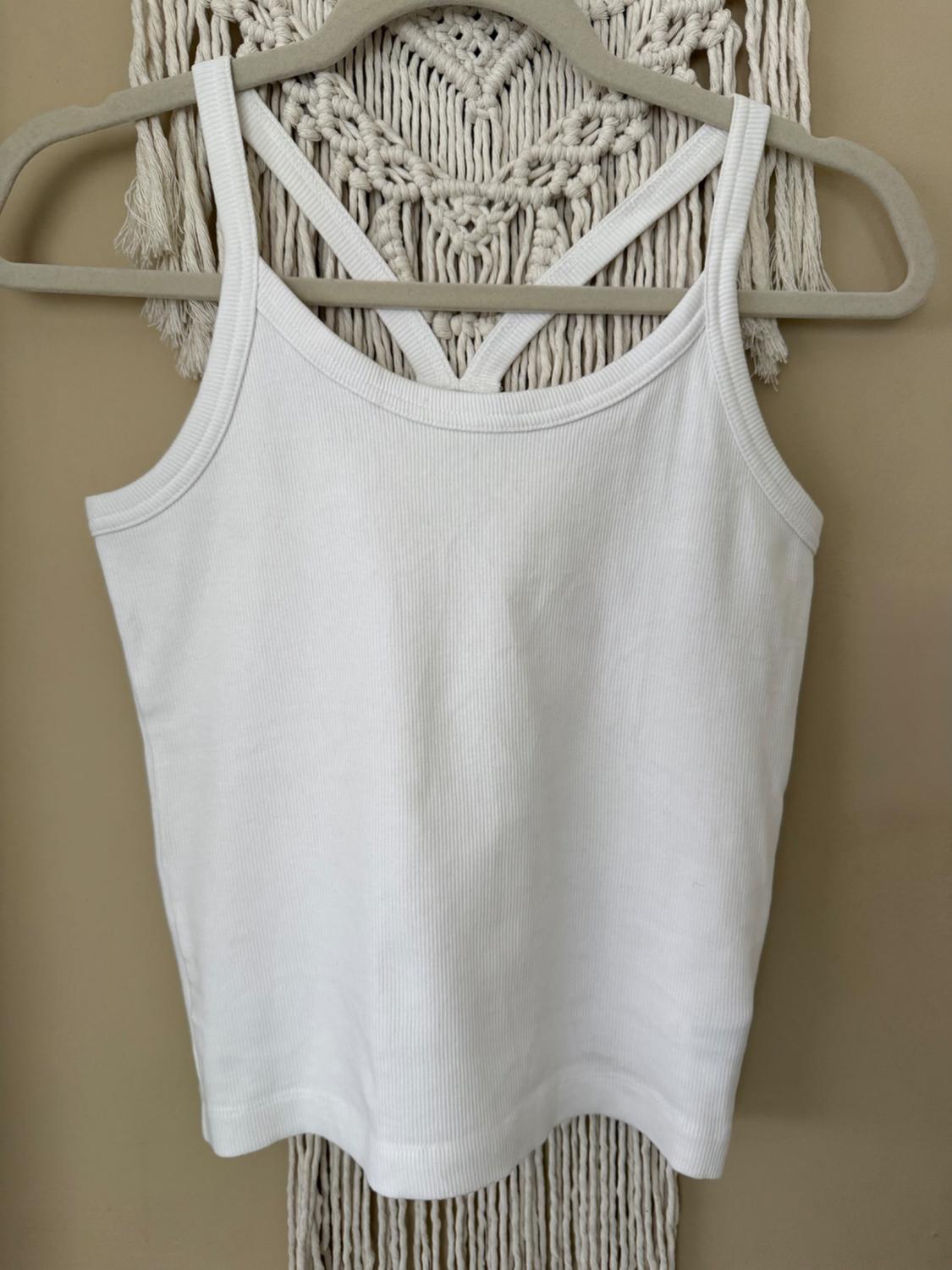 White tank top on a hanger, hanging against a beige macrame background.