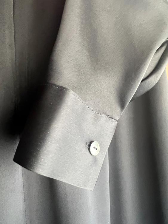 Black shirt sleeve with a buttoned cuff, soft fabric and elegant drape, on a background of the same color.