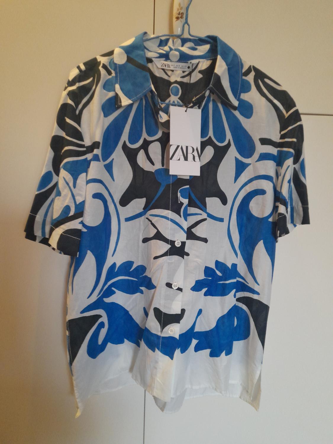 Shirt hanging with a blue and black print on a white background. Visible label with the text "ZARA". White wardrobe background.