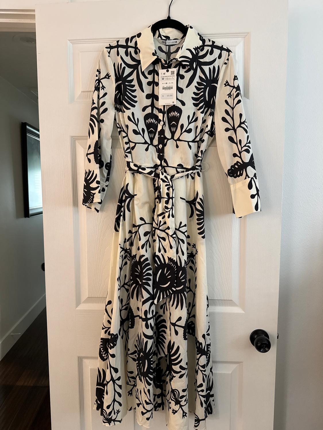 Long dress hanging on a white door, with a black floral print on a white background and a visible label on the collar.
