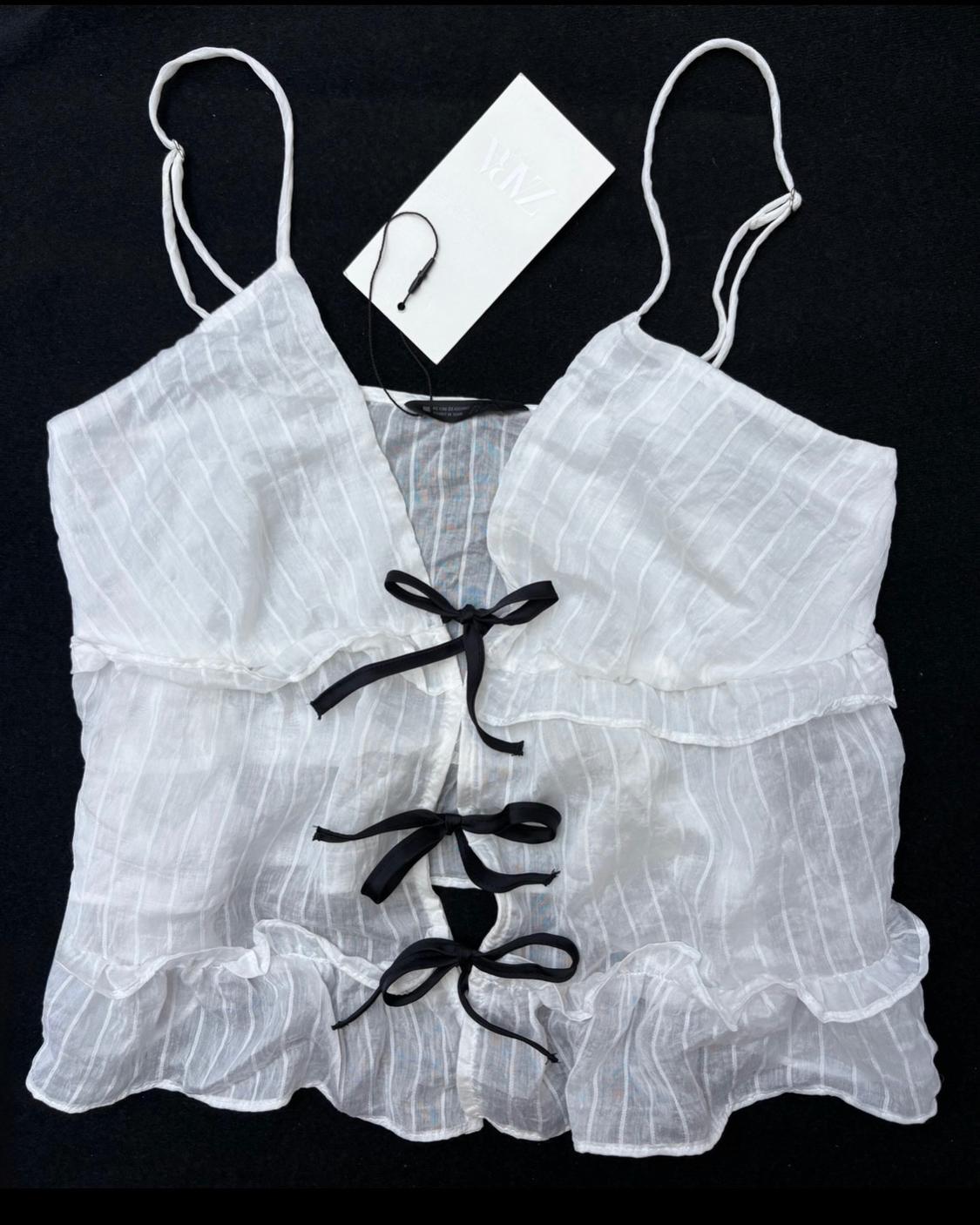 White semi-sheer camisole top with stripes, ruffles and three black bows on the front against a black background. ZARA label.
