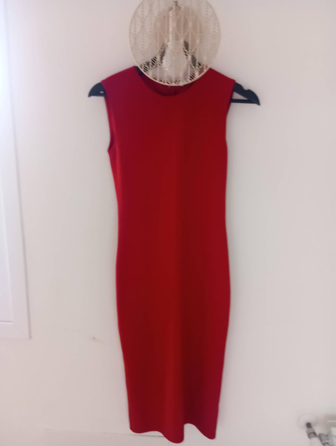 Sleeveless red dress hanging on a black hanger against a white wall.