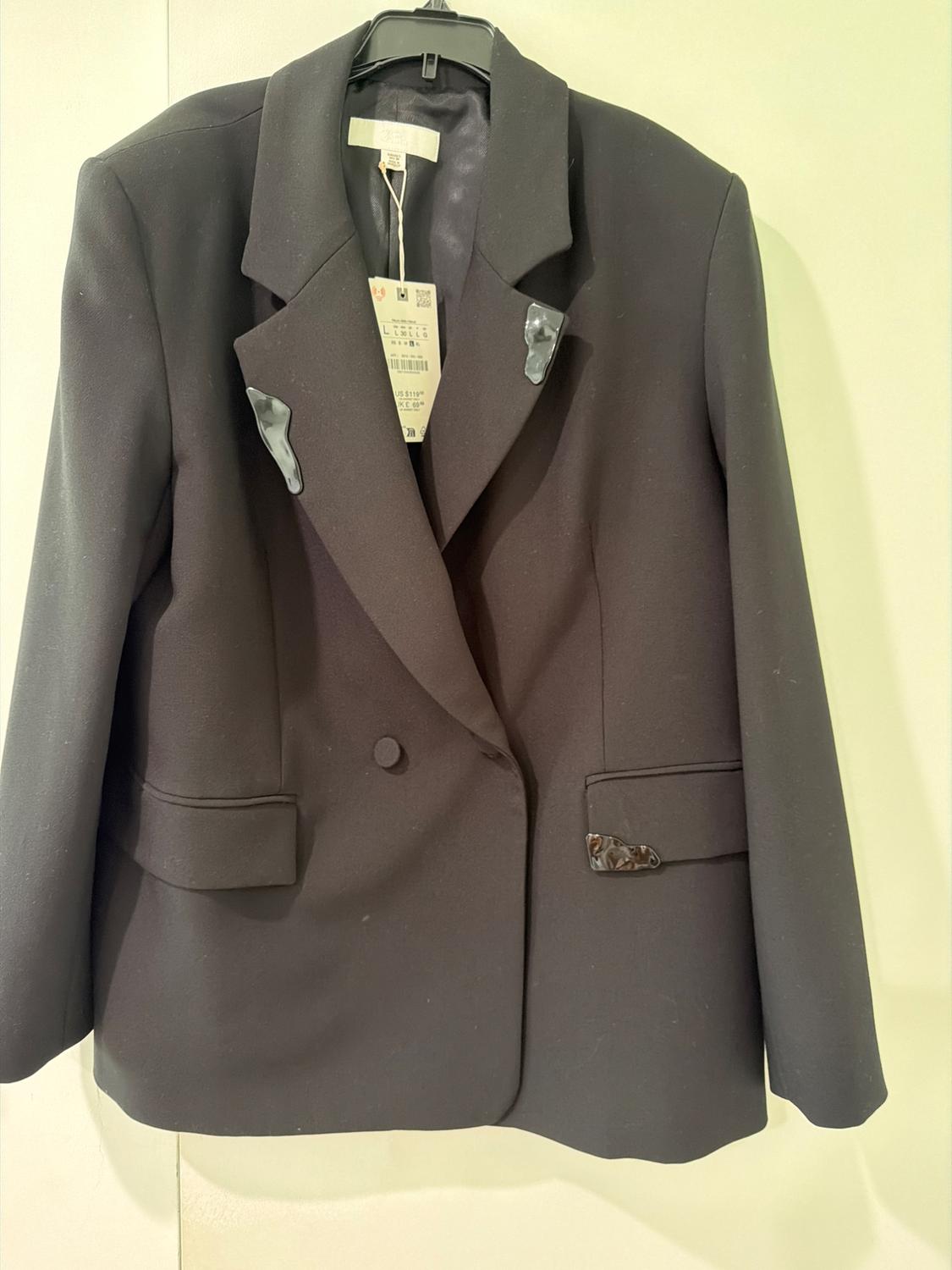 Black blazer on a hanger against a light background. Featuring irregular appliqué details on the lapels and pocket. Label with ZARA text, US $119.