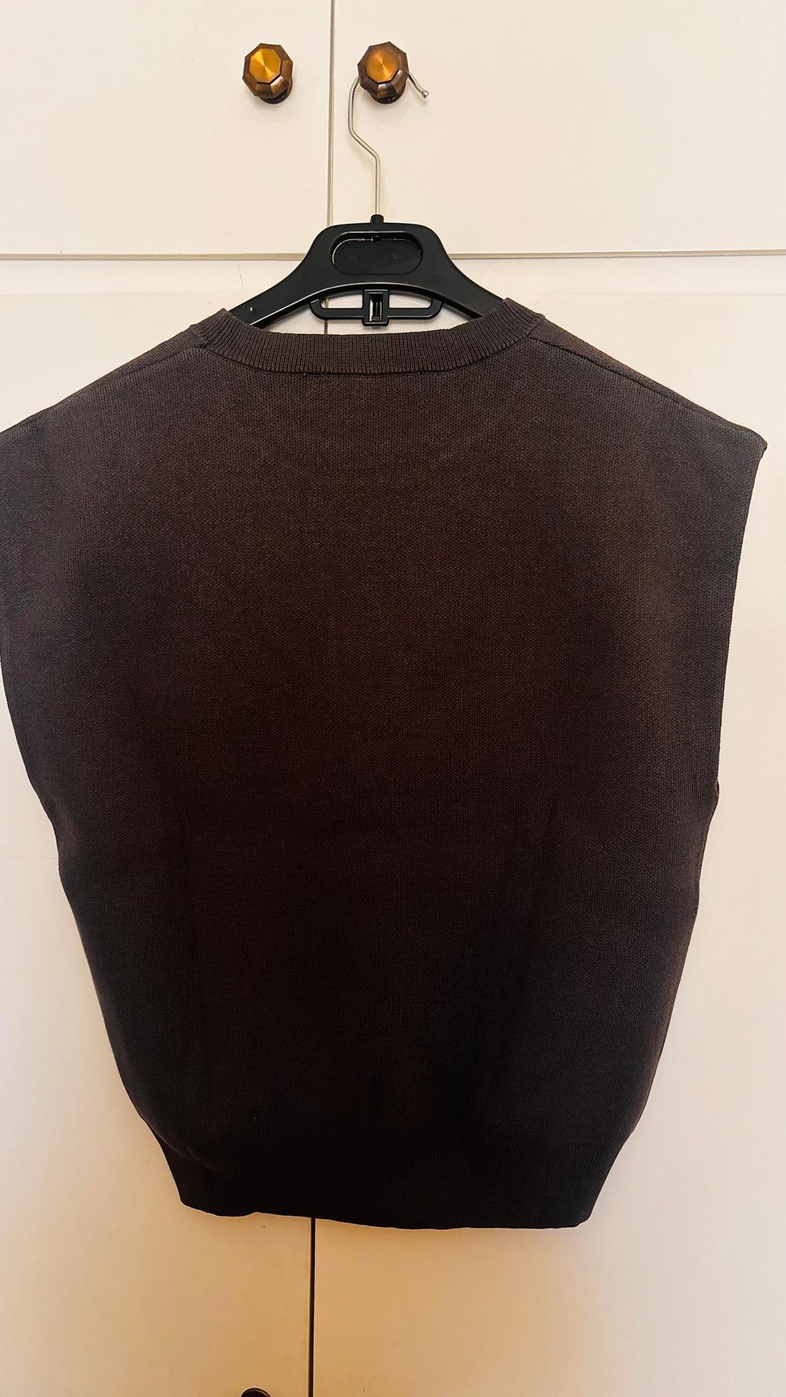 Dark brown waistcoat hanging on a black hanger against a white wardrobe background with gold handles.