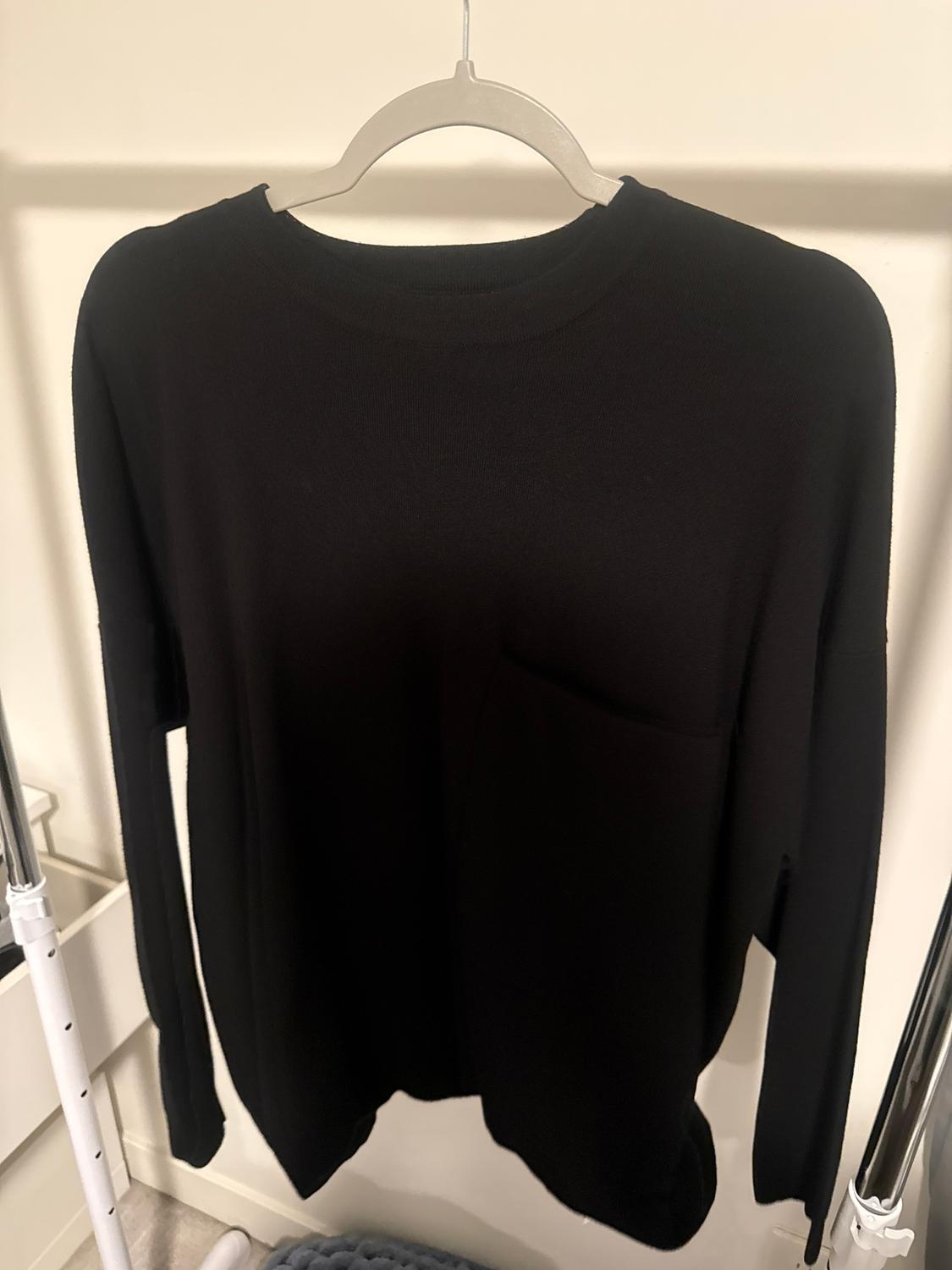 Black long-sleeved jumper hanging on a white hanger, with a light background.