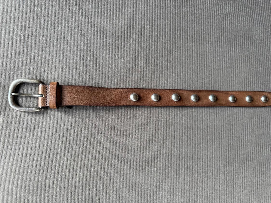 Brown belt with a metal buckle and silver rivets on a textured grey background.