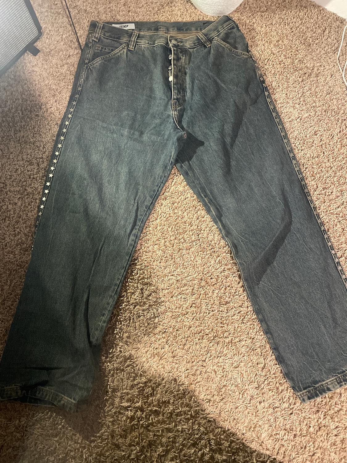 Dark denim jeans with visible buttons and star details on the sides, on a beige rug.