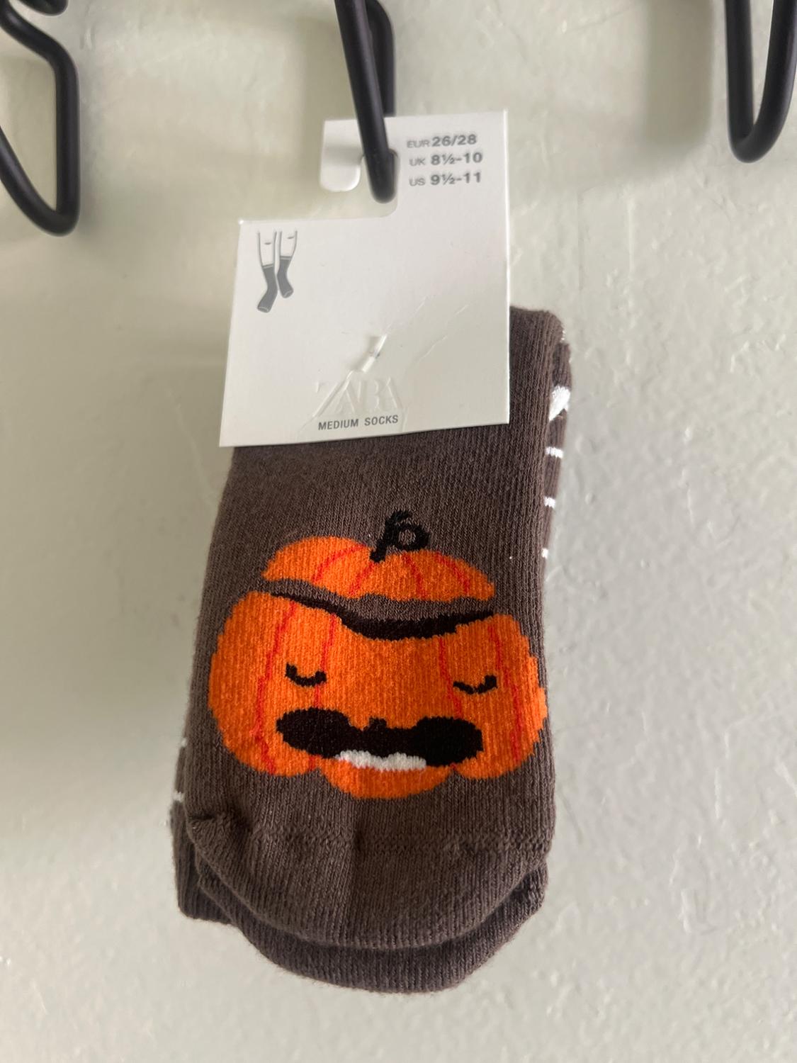 Brown socks with orange pumpkin and moustache design. White label with sizes: EUR 26/28, UK 8½-10, US 9½-11.