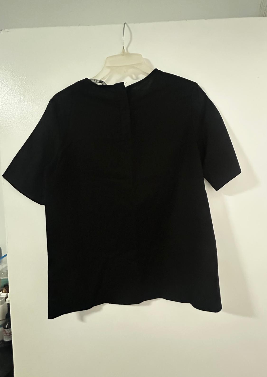 Black short-sleeved t-shirt hanging on a white hanger against a white wall.