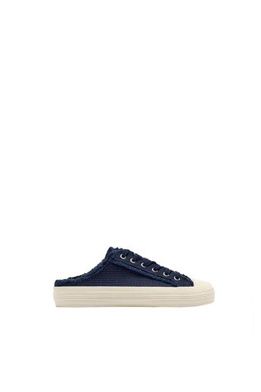 Navy blue backless trainer with white sole on a white background. Casual design with metal eyelets and woven texture.