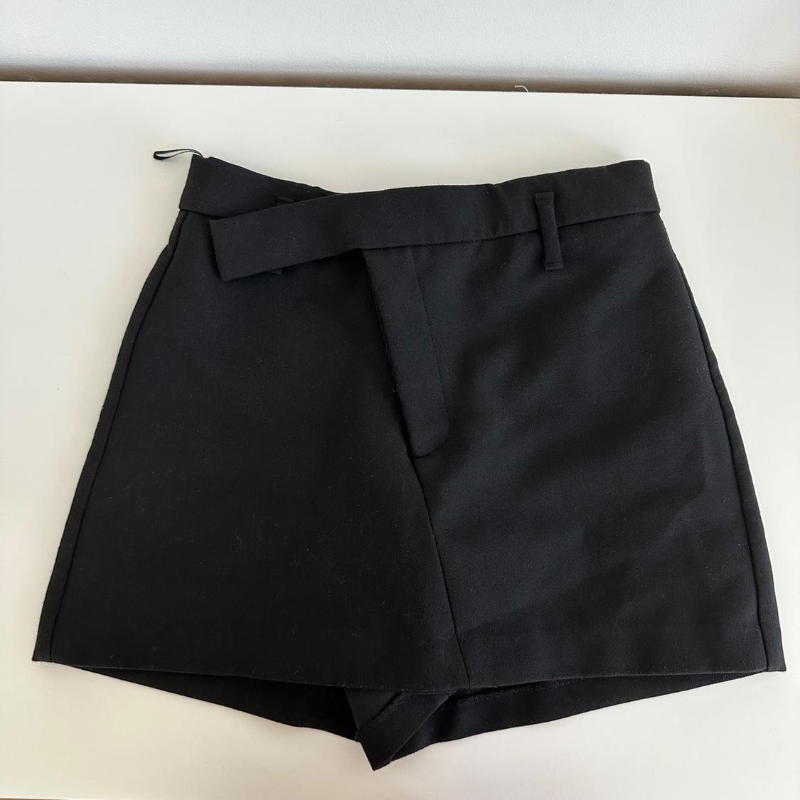 Black shorts with an asymmetric waist detail, on a white surface.