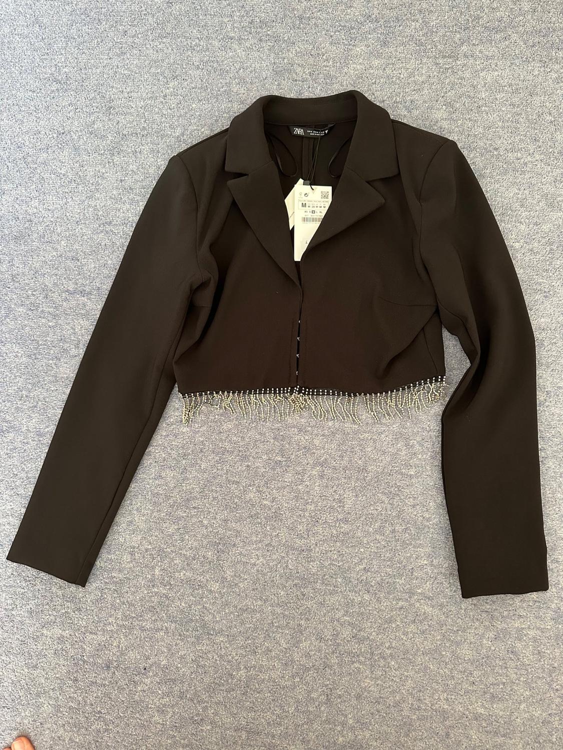 Front view of a black cropped jacket with a lapel and beading details on the hem.
