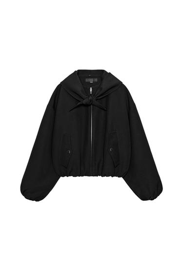 Front view of a black bomber jacket with a round neck and detachable scarf. Front flap pockets with zip fastening.