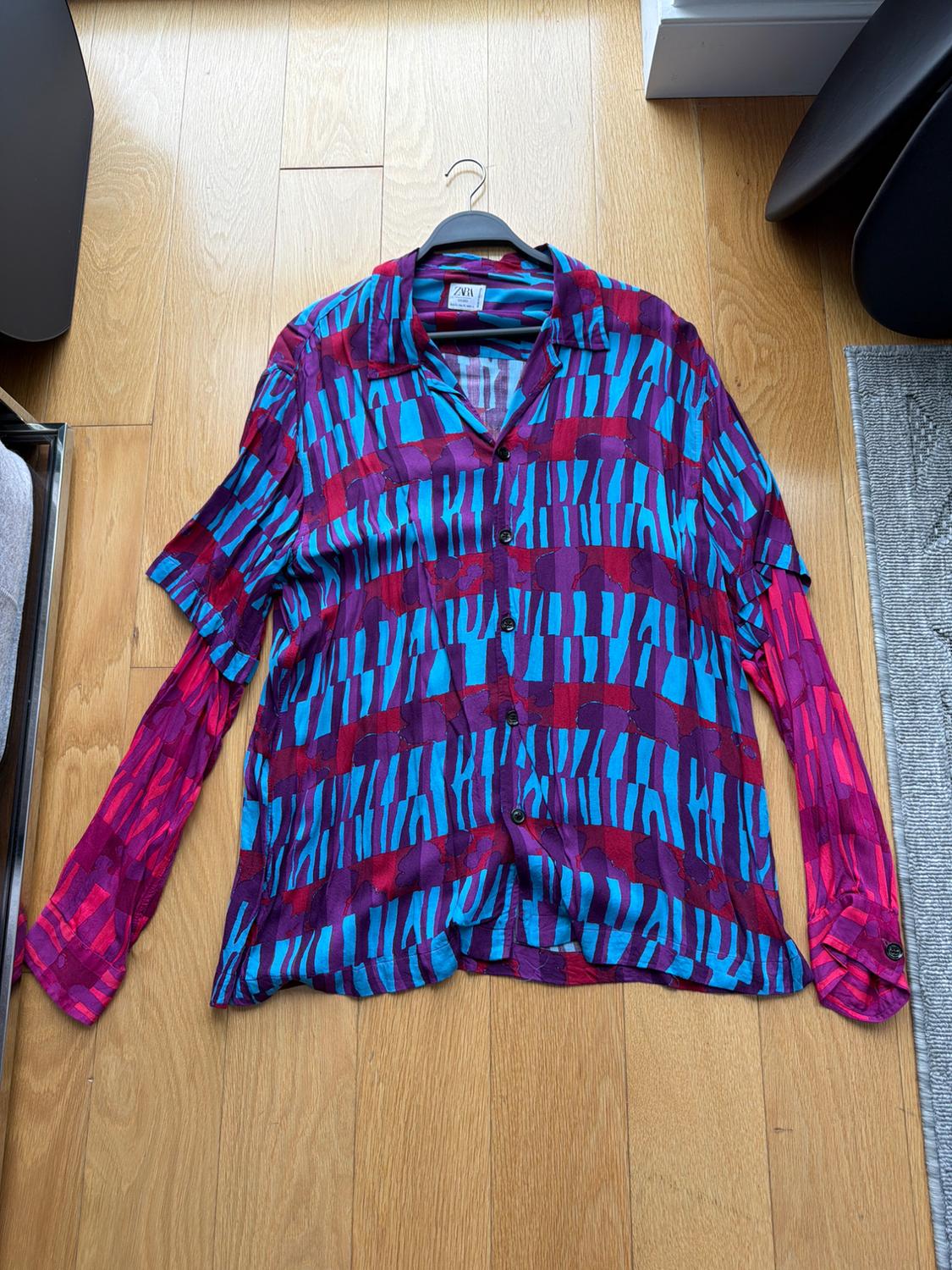 Long-sleeve shirt with geometric print in blue, red, and purple on a wooden floor. Visible tag: ZARA.