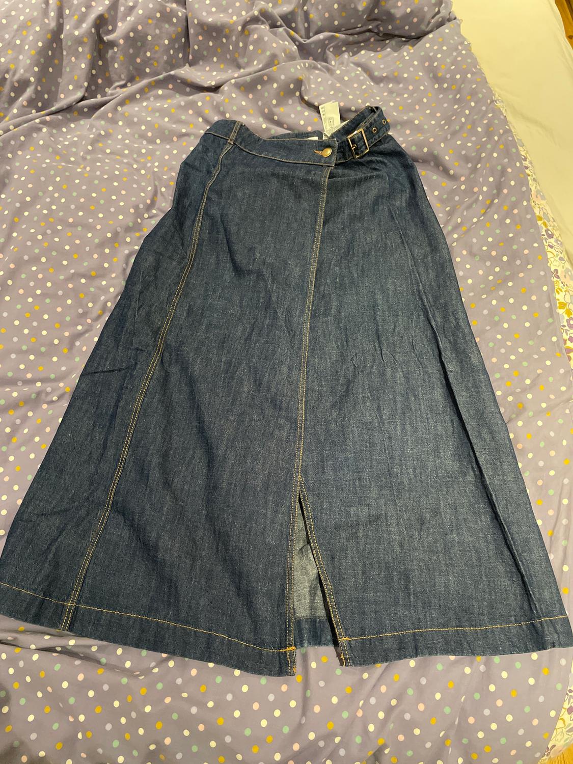 Blue denim skirt with a front split, on a lilac quilt with coloured dots. Visible label on the waistband.