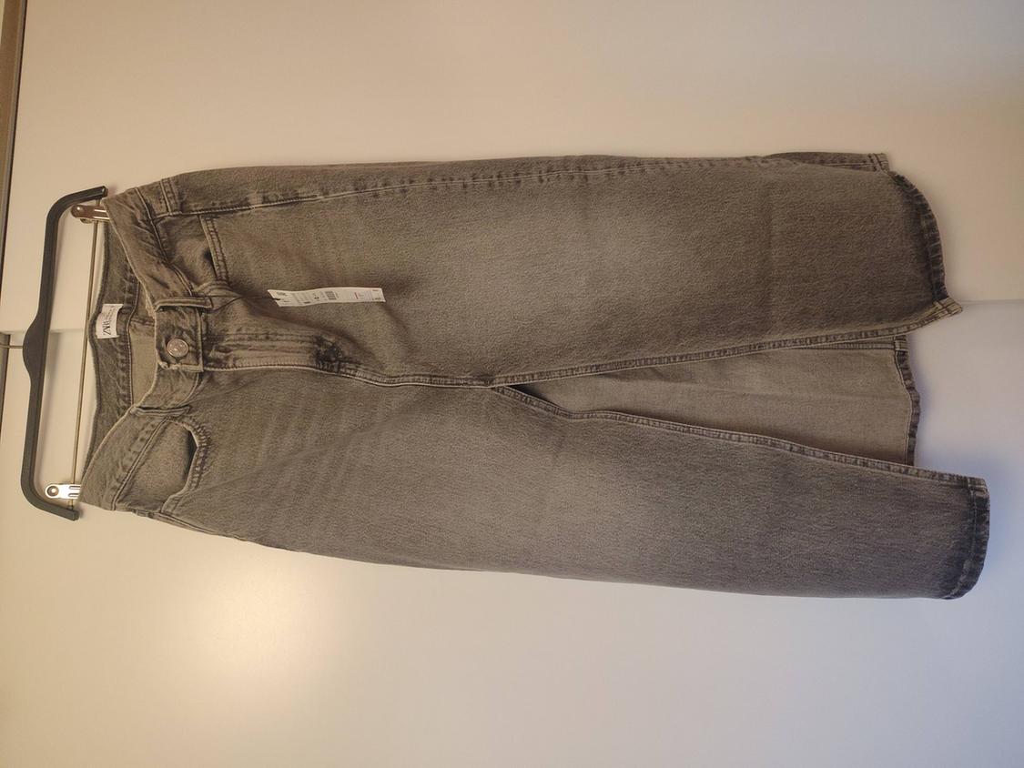 Grey denim skirt with a front slit, hanging on a black hanger against a white surface. Inside label with the text ZARA.