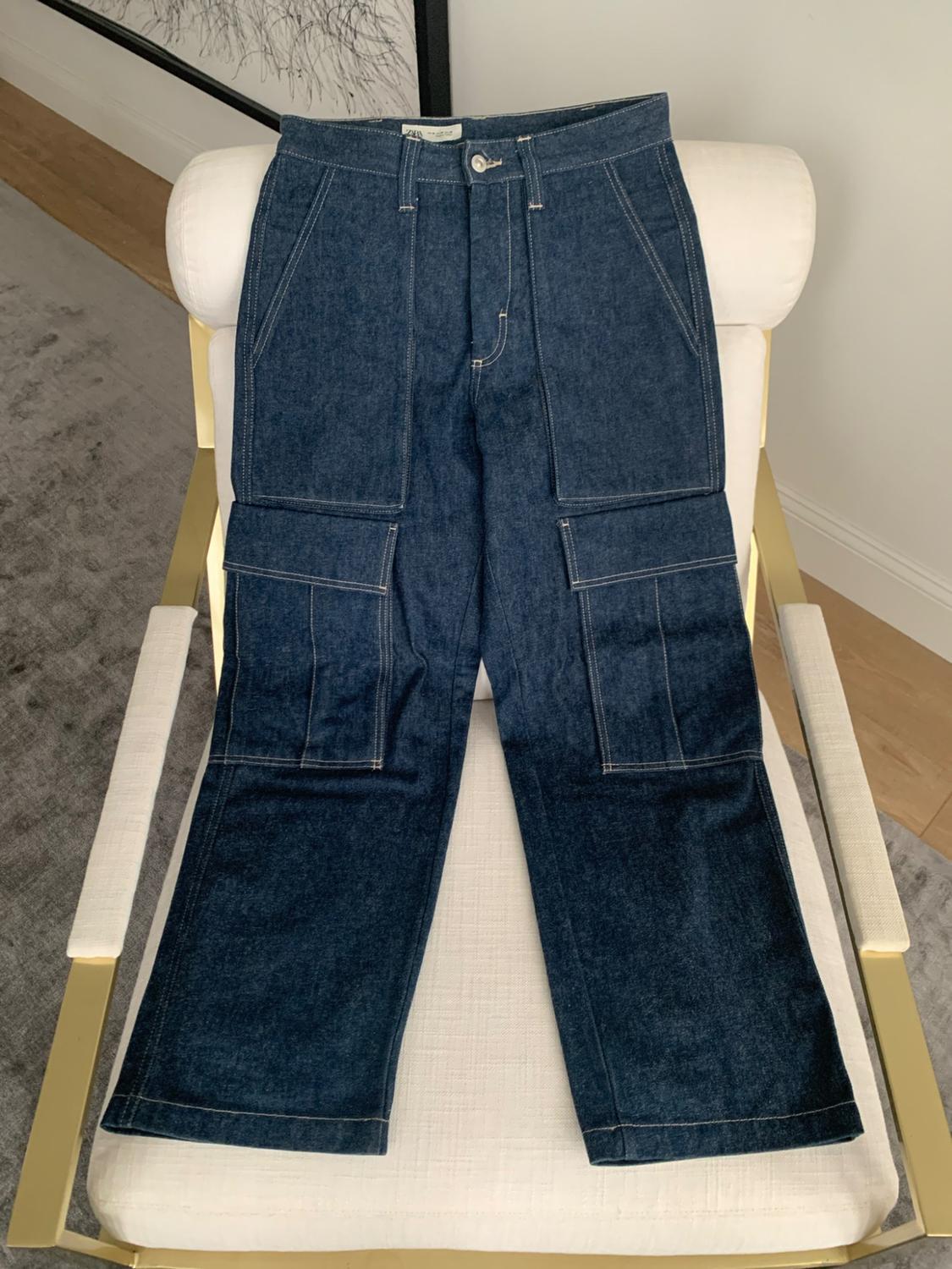 Dark blue cargo jeans with pockets and white stitching, laid on a white chair with a gold frame indoors.