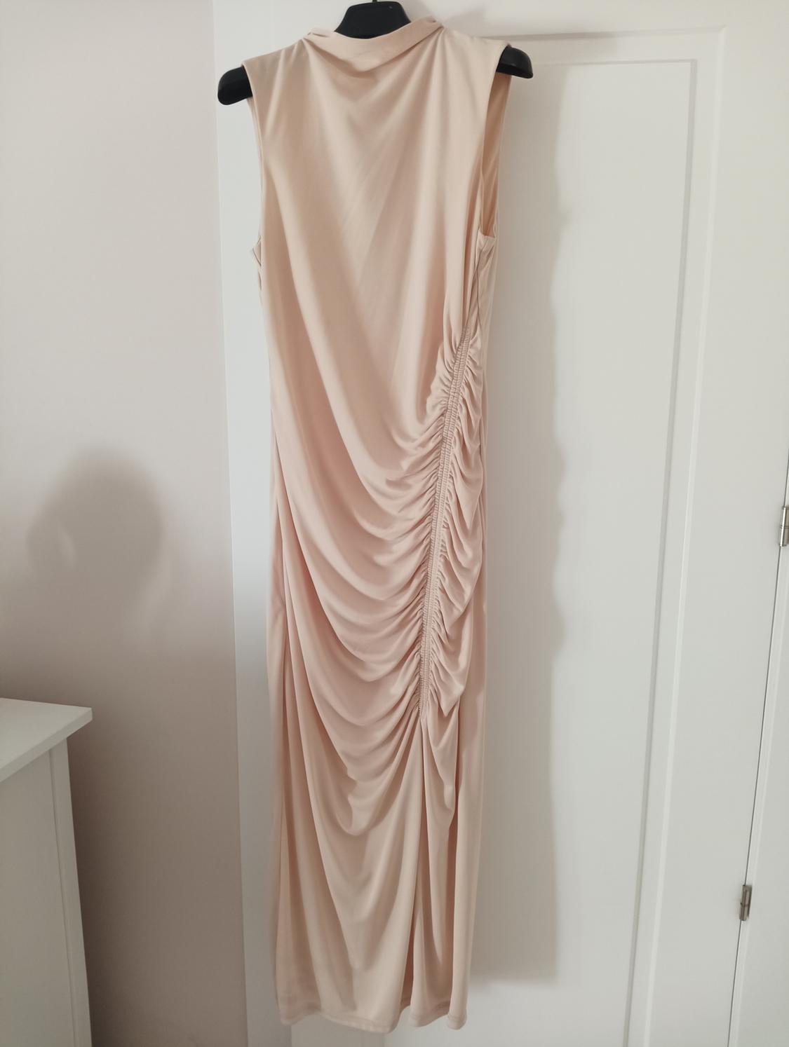 Beige sleeveless maxi dress with side ruching, hanging on a black hanger over a white door.