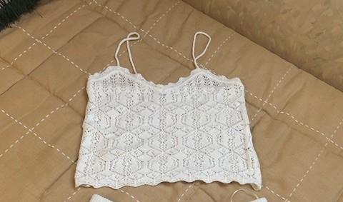 White crochet top with thin straps on a beige bedspread with a checked design.
