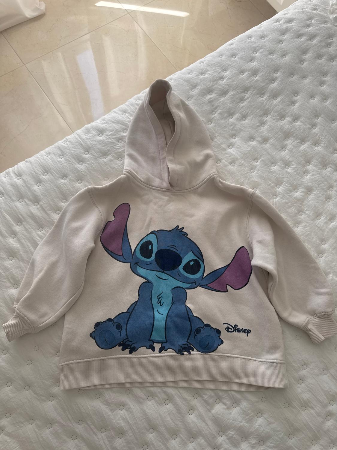 Beige hoodie with blue and purple Disney character print on a white quilted bed.