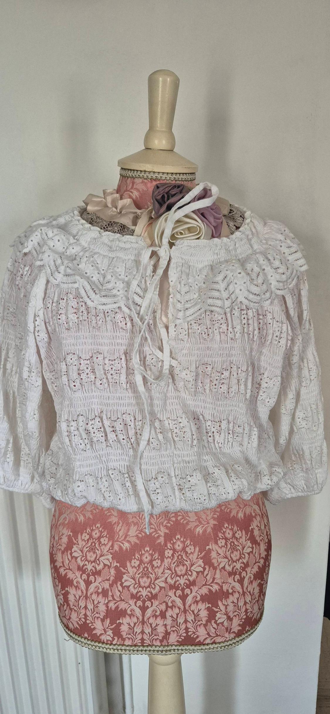 Mannequin with white lace blouse and bows, on a pink fabric base with a floral design. Plain white background.