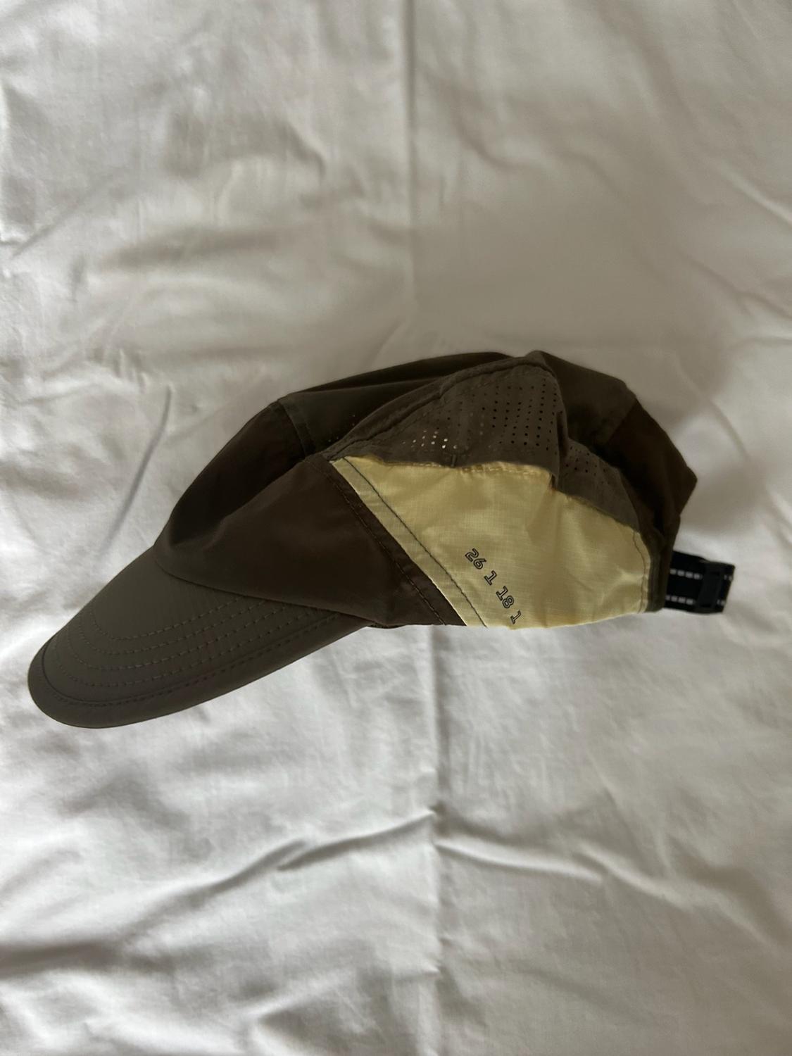 Brown and yellow cap with perforated details and the text “26 1 18 T 92”, resting on a crumpled white cloth.